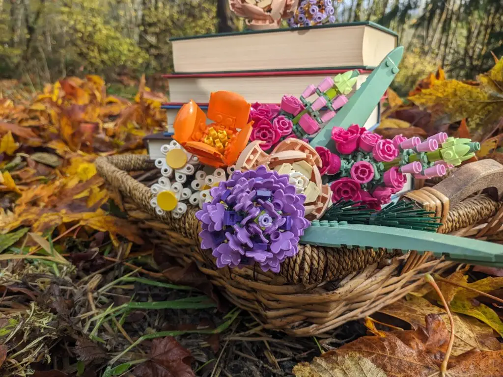 Stack of novels and flowers in a basket. There are fall leaves surrounding the basket.